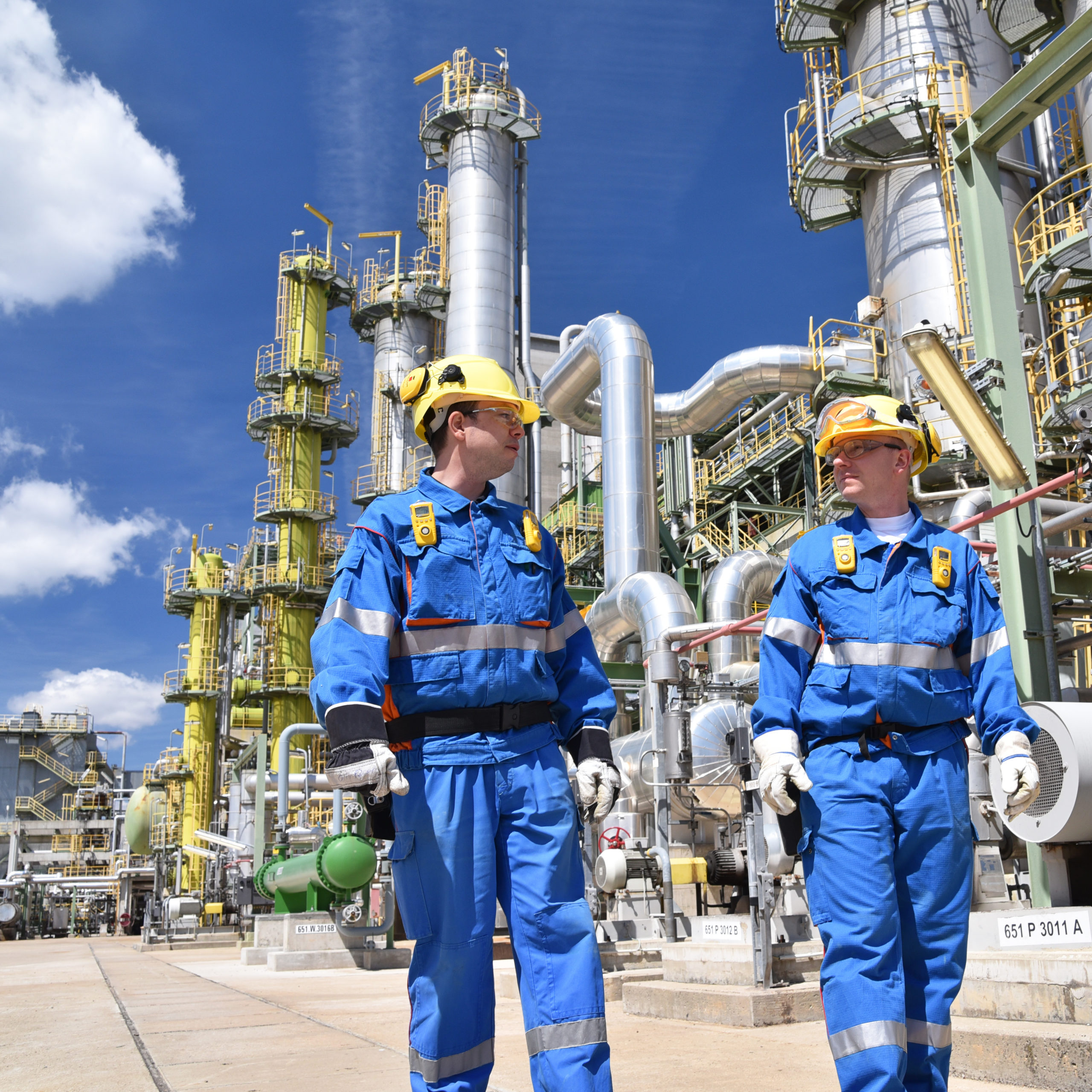 Industriearbeiter in Erdölraffinerie // chemical industry plant - workers in work clothes in a refinery with pipes and machinery